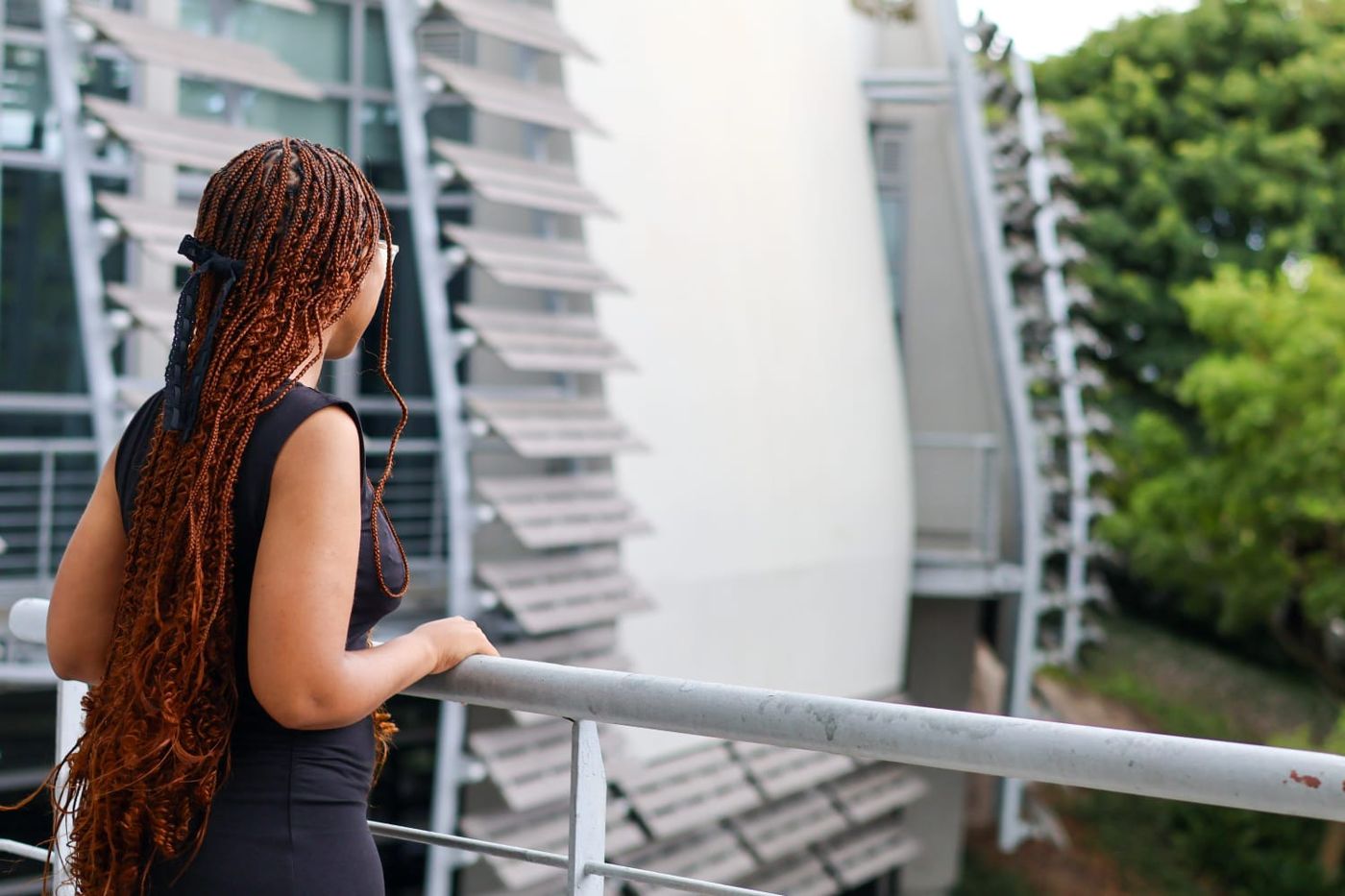Okuhle seen from behind, resting on a railing and looking out at a large modern building and trees